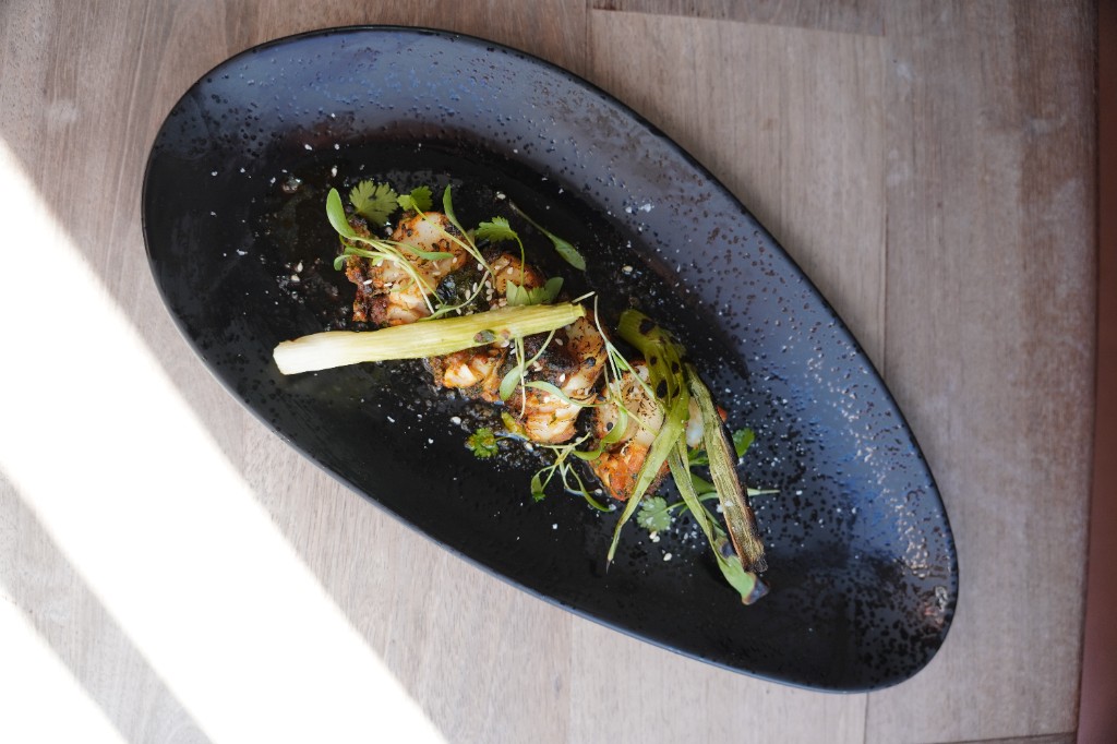 Grilled prawns on black dish with herbs and charred aromatics